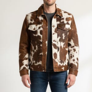 Puede incluir: Chaqueta de piel de vaca marr&oacute;n y blanca con cuello cl&aacute;sico, cierre de botones y dos bolsillos en el pecho. La chaqueta tiene un patr&oacute;n natural y moteado y se usa con vaqueros azules.