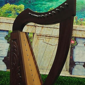 May include: A dark brown wooden harp with strings. The instrument has a decorative carved design on the soundbox and a curved neck. The background shows a scenic landscape.