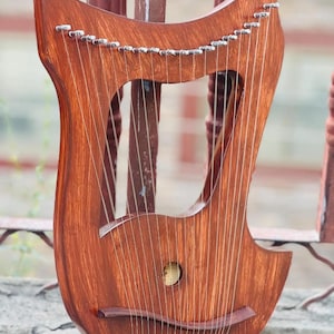 May include: A wooden lyre with a warm brown finish. The instrument has a distinctive curved shape with a central opening and numerous strings. The strings are strung from the top to the bottom of the lyre. The lyre is a musical instrument.