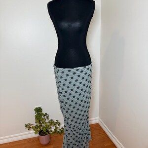 May include: A black dress form displays a light blue skirt with a repeating black floral pattern. The skirt is draped to show its shape and texture. The dress form is on a black stand.