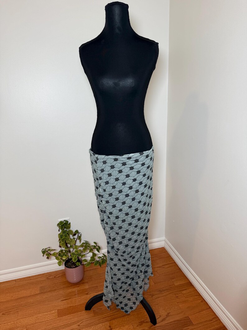 May include: A black dress form displays a light blue skirt with a repeating black floral pattern. The skirt is draped to show its shape and texture. The dress form is on a black stand.
