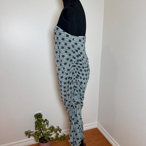 May include: A light blue dress with a black star pattern is displayed on a black dress form. The dress is ruched and has a strapless design. The dress is made of a soft, flowing fabric.
