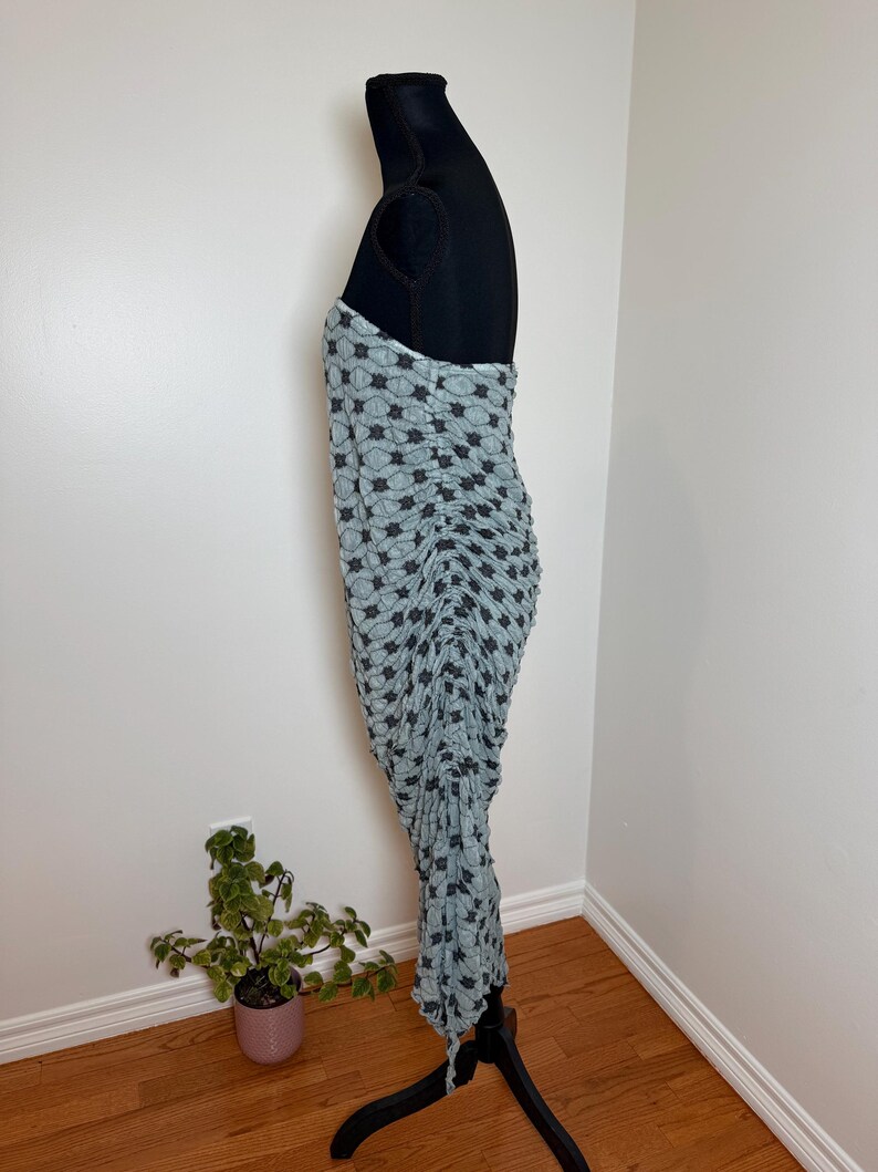 May include: A light blue dress with a black star pattern is displayed on a black dress form. The dress is ruched and has a strapless design. The dress is made of a soft, flowing fabric.