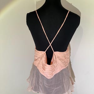 May include: A light pink camisole top with spaghetti straps and a low back. The top features a ruched bodice and a flowing, sheer skirt. The garment is displayed on a black mannequin.