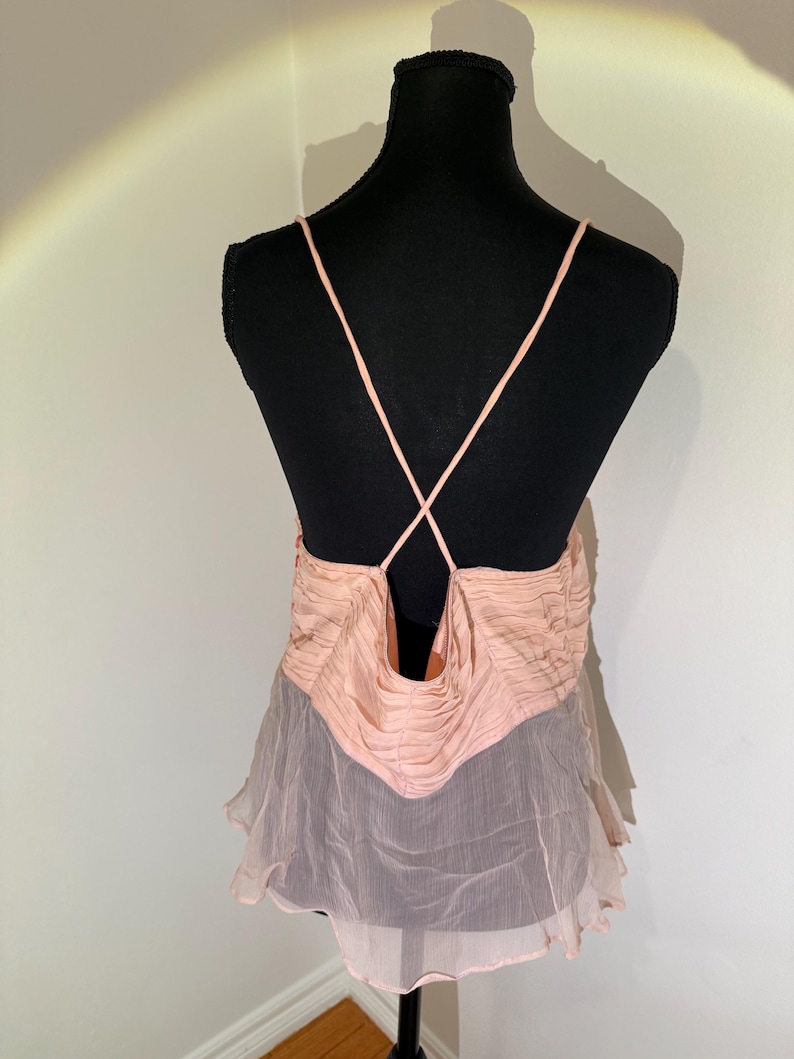 May include: A light pink camisole top with spaghetti straps and a low back. The top features a ruched bodice and a flowing, sheer skirt. The garment is displayed on a black mannequin.