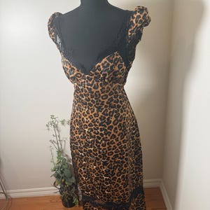 Puede incluir: Un vestido con estampado de leopardo con adornos y detalles de encaje negro. El vestido se exhibe en un maniqu&iacute; negro. El vestido tiene un escote en V y mangas cortas. El vestido llega a la rodilla.
