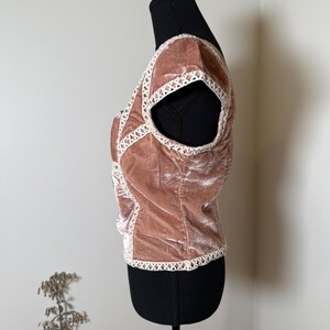 Puede incluir: Top de terciopelo rosa empolvado con ribete de encaje blanco. La parte superior de manga corta presenta un dise&ntilde;o entrecruzado en la parte delantera y alrededor de las sisas. La parte superior se muestra en un maniqu&iacute; negro.