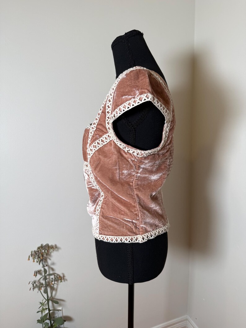 Puede incluir: Top de terciopelo rosa empolvado con ribete de encaje blanco. La parte superior de manga corta presenta un dise&ntilde;o entrecruzado en la parte delantera y alrededor de las sisas. La parte superior se muestra en un maniqu&iacute; negro.