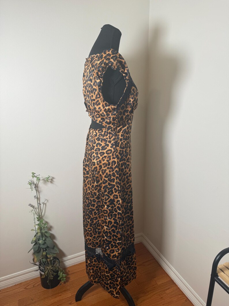 Puede incluir: Vestido largo con estampado de leopardo y ribete de encaje negro en el bajo. El vestido se exhibe en un maniqu&iacute; negro. El vestido presenta un dise&ntilde;o recortado en la cintura y una parte superior sin mangas.