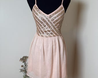 May include: A light pink dress with a sequined bodice and spaghetti straps. The bodice features a V-neck and a gold sequin design. The skirt is a flowing, light pink fabric. The dress is displayed on a black mannequin.