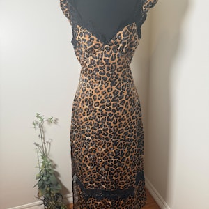 Puede incluir: Un vestido con estampado de leopardo con ribete de encaje negro. El vestido presenta un escote en V, tirantes y una silueta ajustada. El vestido se exhibe en un maniqu&iacute; negro.