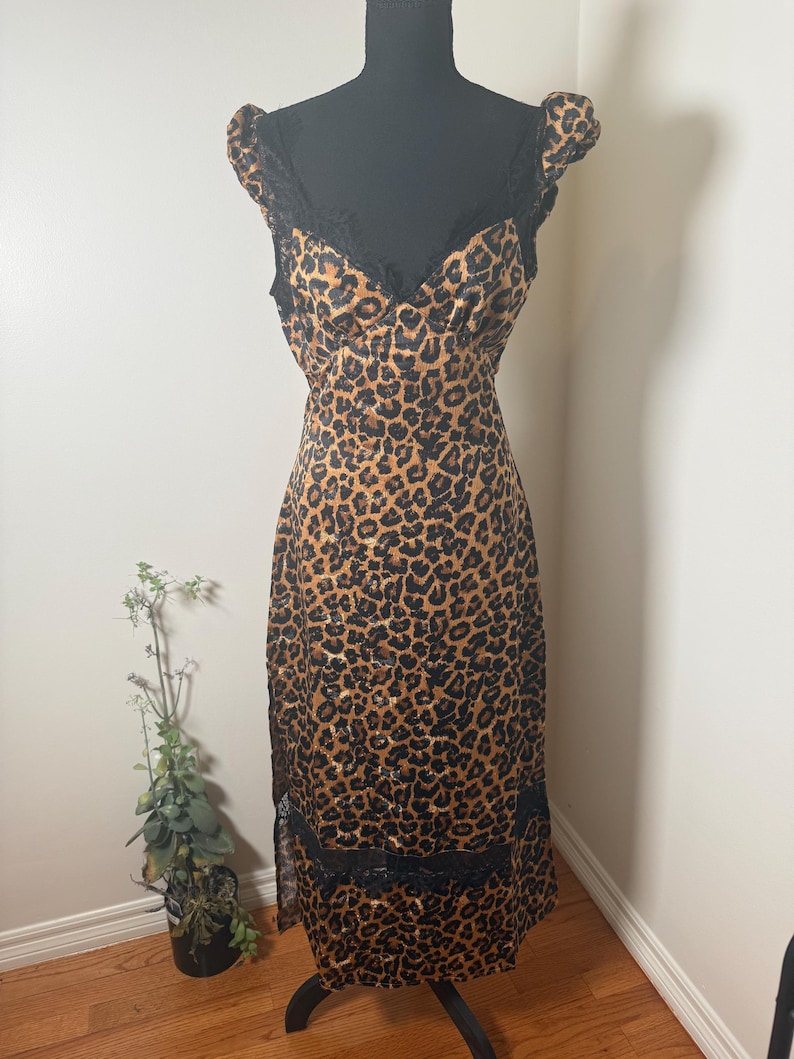 Puede incluir: Un vestido con estampado de leopardo con ribete de encaje negro. El vestido presenta un escote en V, tirantes y una silueta ajustada. El vestido se exhibe en un maniqu&iacute; negro.