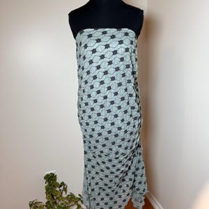 May include: A light blue strapless dress with a black floral pattern, displayed on a black mannequin. The dress features a textured, pleated design and a floor-length, asymmetrical hemline. The dress is made of a lightweight fabric.