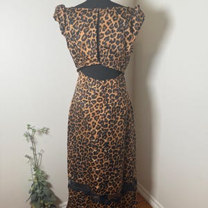 Puede incluir: Un vestido con estampado de leopardo con la espalda descubierta y ribete de encaje negro en el dobladillo. El vestido se exhibe en un maniqu&iacute; negro. El vestido presenta un estampado de manchas marrones y negras.