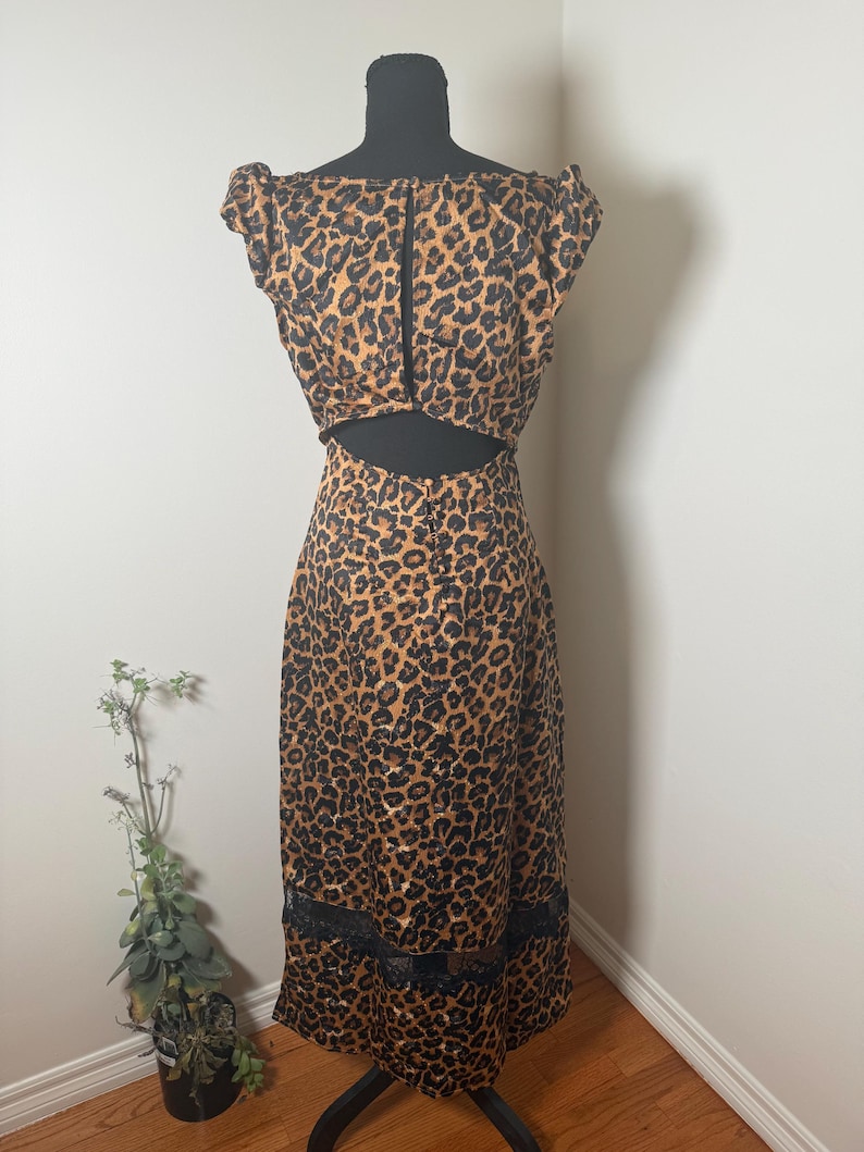 Puede incluir: Un vestido con estampado de leopardo con la espalda descubierta y ribete de encaje negro en el dobladillo. El vestido se exhibe en un maniqu&iacute; negro. El vestido presenta un estampado de manchas marrones y negras.