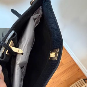 May include: Black tote bag with gold-tone hardware, including a chain strap and clasp closure. The interior is lined with a light-colored material. The bag has a textured exterior.