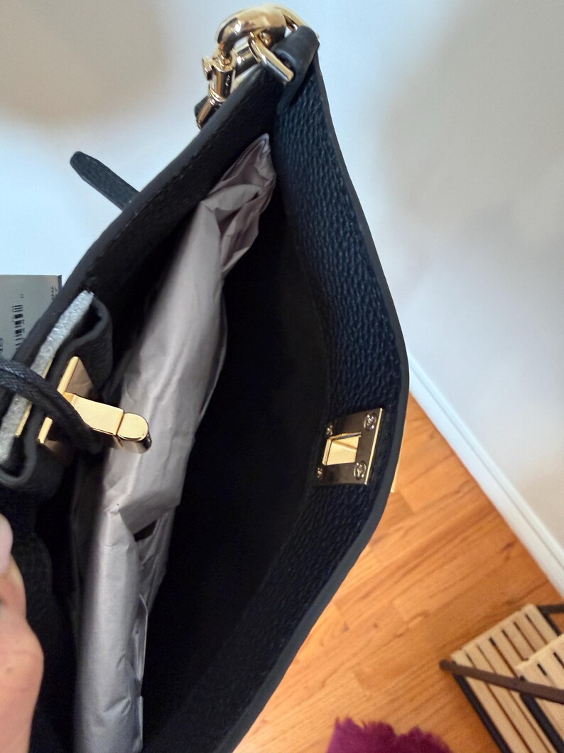 May include: Black tote bag with gold-tone hardware, including a chain strap and clasp closure. The interior is lined with a light-colored material. The bag has a textured exterior.