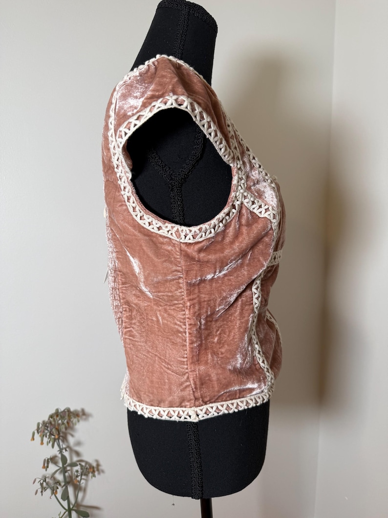 Puede incluir: Top de terciopelo rosa empolvado con ribete de ganchillo blanco. El top sin mangas se muestra en un maniqu&iacute; negro. El ribete de ganchillo perfila el escote, las sisas y el dobladillo inferior del top. La tela de terciopelo tiene un aspecto suave y texturizado.