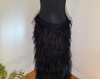 May include: A black, layered tulle skirt. The skirt is displayed on a mannequin, showcasing multiple tiers of ruffled fabric. The skirt's design creates a full, flowing silhouette. The skirt is made of a sheer, lightweight material.