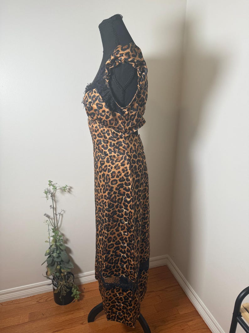Puede incluir: Vestido con estampado de leopardo con ribete de encaje negro y mangas con volantes. El vestido se exhibe en un maniqu&iacute; negro. El vestido tiene un escote redondo y una silueta ajustada. El vestido est&aacute; hecho de una tela ligera.