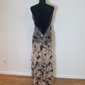 Puede incluir: Un vestido largo y transparente con estampado de mariposas. El vestido presenta un corpi&ntilde;o negro con espalda cruzada y ribete de encaje. La falda es de color beige claro con dise&ntilde;os de mariposas y flores negras.