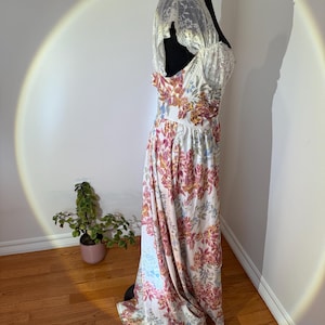 May include: A vintage-style floral print dress on a black mannequin. The dress features a white base with a colorful floral pattern in shades of pink, orange, and blue. The bodice has lace detailing, and the dress appears to be floor-length.