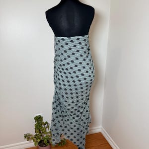 May include: A light blue wrap skirt with a black star pattern is draped on a black mannequin. The skirt is made of a textured fabric and hangs to the floor. The mannequin is on a black stand.