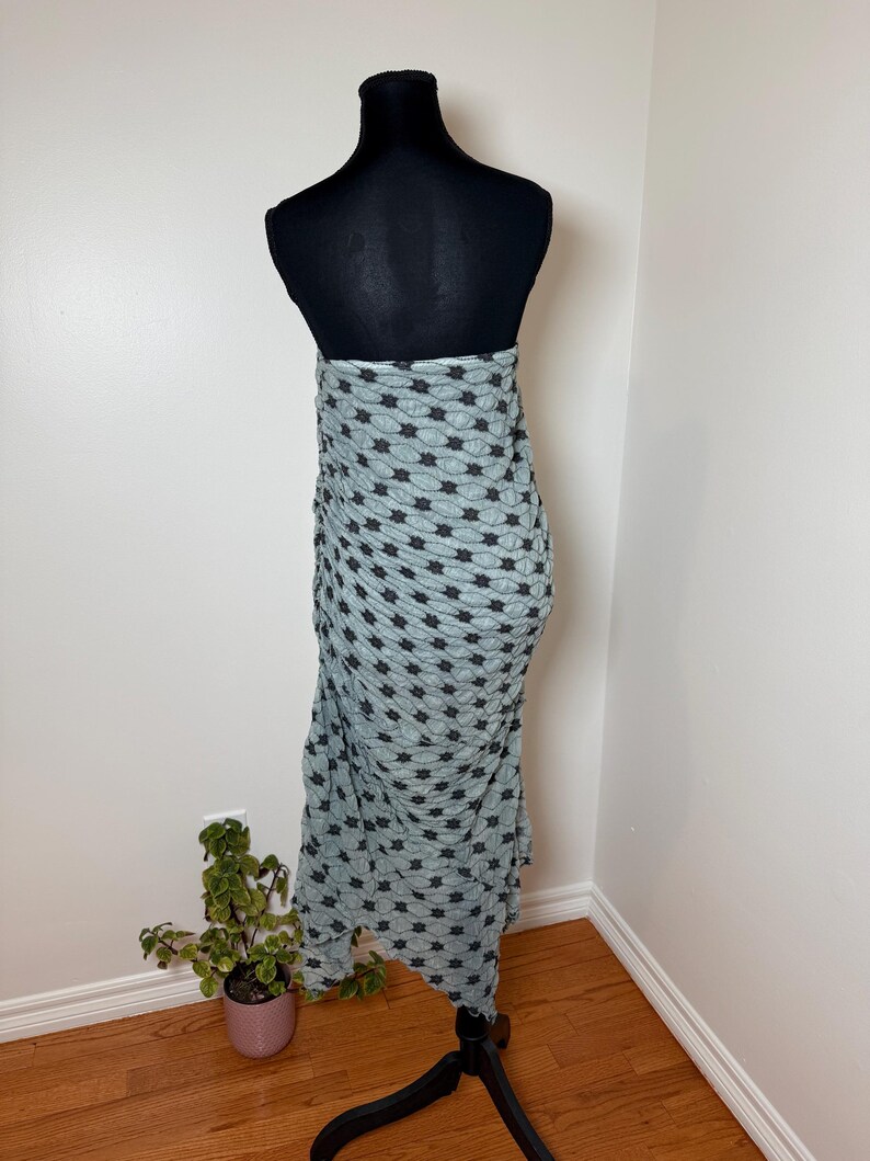 May include: A light blue wrap skirt with a black star pattern is draped on a black mannequin. The skirt is made of a textured fabric and hangs to the floor. The mannequin is on a black stand.