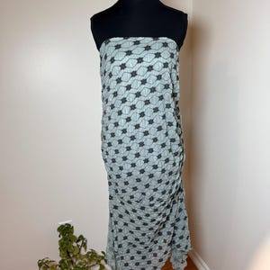May include: A pale blue strapless dress featuring a black floral design. The dress is shown on a black mannequin and has a draped, textured look. The floor-length dress has a ruffled hem.