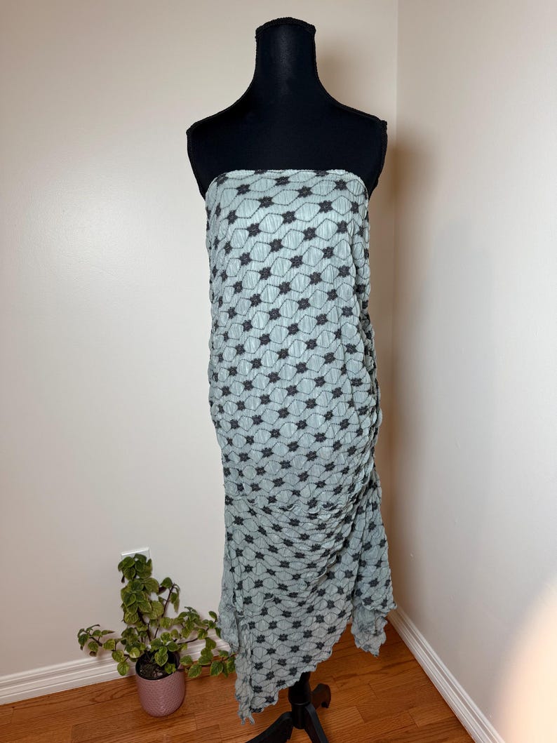 May include: A pale blue strapless dress featuring a black floral design. The dress is shown on a black mannequin and has a draped, textured look. The floor-length dress has a ruffled hem.