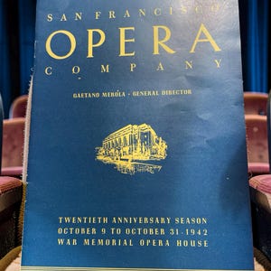 May include: A dark blue San Francisco Opera Company program from the 1942 twentieth anniversary season. The cover features gold text and a gold illustration of the War Memorial Opera House, with Gaetano Merola listed as general director.