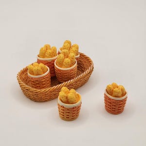 May include: A miniature wicker basket tray holds several small orange baskets filled with yellow, textured food items. One basket sits separately. The baskets have a white rim and are arranged on a white surface.