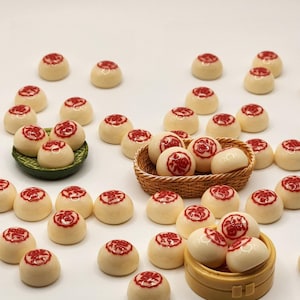 May include: An overhead shot displays numerous small, round, off-white objects with a red symbol on top. Some are scattered, while others are arranged in small green, brown, and tan containers. The objects are likely decorative or edible.