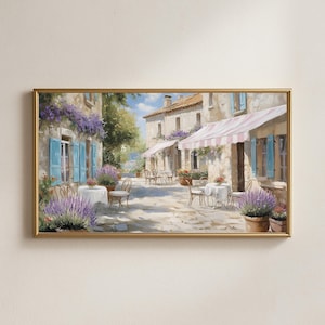 May include: A framed painting depicts a European street scene with cafes. The artwork features stone buildings, blue shutters, and tables with white tablecloths. Lavender plants in pots and hanging from the buildings add color.