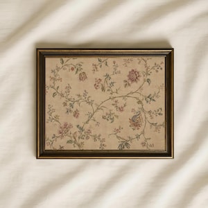 Puede incluir: Una pieza de arte mural rectangular con un marco de bronce oscuro que rodea un estampado beige con un patrón floral repetitivo. El diseño muestra enredaderas delicadas y sinuosas con hojas pequeñas y flores en tonos rosa, azul y verde.