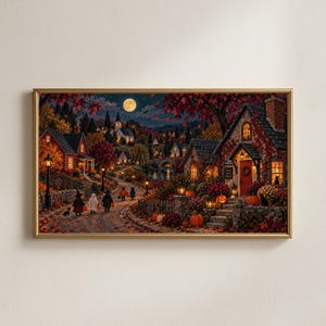 May include: A rectangular framed wall art print depicting a nighttime autumn village scene with a full moon, glowing street lamps, and houses decorated with pumpkins. Children in costumes walk along a path covered in fallen red and orange leaves.