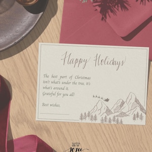Pode incluir: Um postal de Natal com o texto "CHRISTMAS POSTCARD" e "USE DIGITALLY OR PRINTED". O postal tem uma mensagem que diz "Happy Holidays" e um desenho de montanhas e árvores. Enfeites dourados e um envelope vermelho também são visíveis.