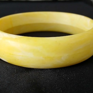 May include: A yellow bangle bracelet with a marbled effect. The bracelet is a light yellow colour with white marbling. The bracelet is circular and appears to be made of a solid material.