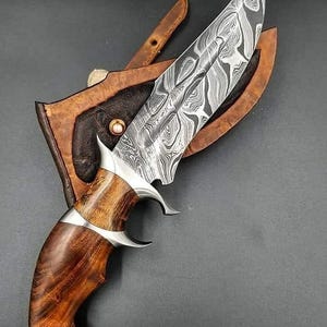 Puede incluir: Cuchillo de caza de acero de Damasco con mango de madera y funda de cuero. La hoja tiene un patr&oacute;n &uacute;nico y el mango es de color marr&oacute;n oscuro. El cuchillo est&aacute; dise&ntilde;ado para uso en exteriores y supervivencia.