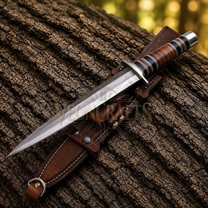 Può includere: Un pugnale artigianale con una lama in acciaio lucido e un manico avvolto in pelle marrone e nera. Il pugnale è in un fodero di cuoio marrone, con il testo "VEON CRAFTS" visibile. Il coltello è esposto su una superficie marrone strutturata.