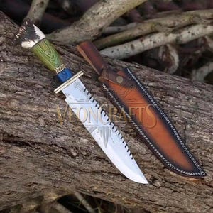 Puede incluir: Un cuchillo de hoja fija con una hoja de acero plateado con diseño grabado, un mango de madera verde y azul, y un pomo de asta texturizado. El cuchillo viene con una funda de cuero marrón con costuras blancas y un cierre de botón metálico.
