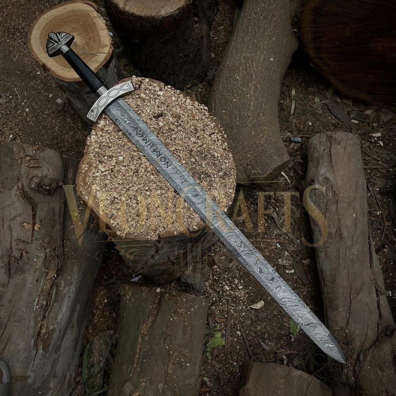 Puede incluir: Vista cenital detallada de una espada con una hoja estampada y un mango negro. La espada descansa sobre una superficie de madera, rodeada de troncos. La hoja tiene texto grabado. El dise&ntilde;o sugiere un tema hist&oacute;rico o de fantas&iacute;a.