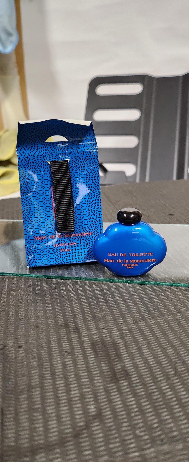 Pu&ograve; includere: Un flacone di profumo Eau de Toilette blu con un tappo nero accanto a una scatola blu con un cinturino nero. La bottiglia e la scatola hanno testo bianco. La bottiglia ha la forma di una nuvola.