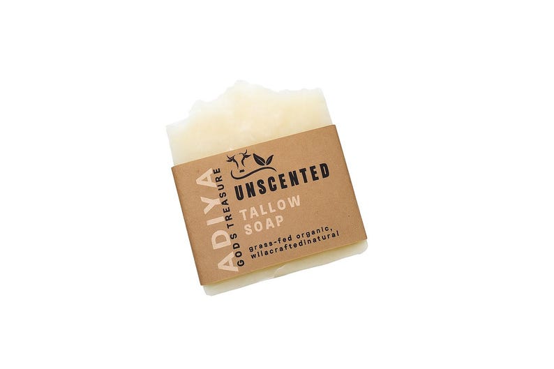 Peut inclure: Un pain de savon au suif non parfum&eacute; avec une &eacute;tiquette en papier brun. L'&eacute;tiquette indique "ADIYA GODS TREASURE UNSCENTED TALLOW SOAP" avec du texte suppl&eacute;mentaire indiquant qu'il est biologique nourri &agrave; l'herbe et naturel sauvage.