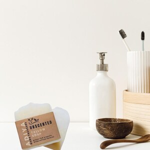 Peut inclure: Nature morte pr&eacute;sentant un savon au suif non parfum&eacute; avec une &eacute;tiquette marron, un distributeur de savon blanc, un bol en bois et une cuill&egrave;re en bois. Deux brosses &agrave; dents sont dans un porte-brosse &agrave; dents en c&eacute;ramique blanche. Le savon est &eacute;tiquet&eacute; "ADIYA GODS TREASURE".