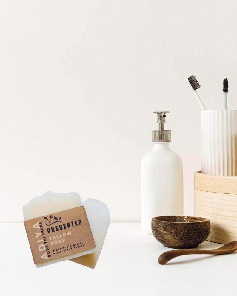 Peut inclure: Nature morte pr&eacute;sentant un savon au suif non parfum&eacute; avec une &eacute;tiquette marron, un distributeur de savon blanc, un bol en bois et une cuill&egrave;re en bois. Deux brosses &agrave; dents sont dans un porte-brosse &agrave; dents en c&eacute;ramique blanche. Le savon est &eacute;tiquet&eacute; "ADIYA GODS TREASURE".