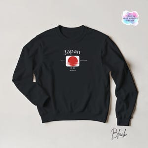 May include: Black sweatshirt featuring a graphic of the Japanese flag with the word "Japan" above a red sun design. The sweatshirt also includes the text "EST 660BCE" and Japanese characters. The word "Black" is written in cursive at the bottom.