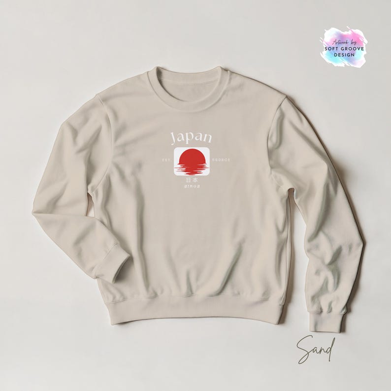May include: Sand-colored sweatshirt with a crew neck. The front features a graphic of a red sun over water within a white square, with the word "Japan" above. The sweatshirt also has the text "EST. since" and "PRODUCT" on the front.