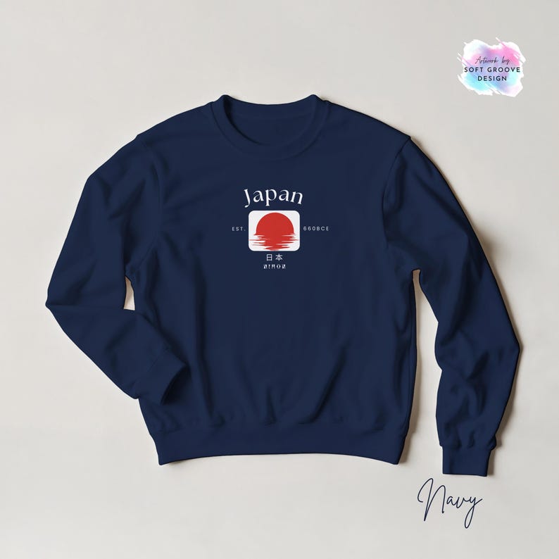 May include: Navy blue sweatshirt featuring a graphic design with the word "Japan" in white, a red sun, and Japanese text. The sweatshirt has a crew neck and long sleeves. The design includes the text "EST 660BCE".