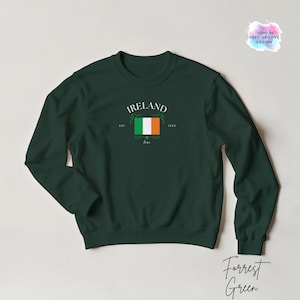 May include: A dark green sweatshirt with the word "IRELAND" above a graphic of the Irish flag. The sweatshirt has a crew neck and long sleeves. The text "Est. 1923" is also included in the design.
